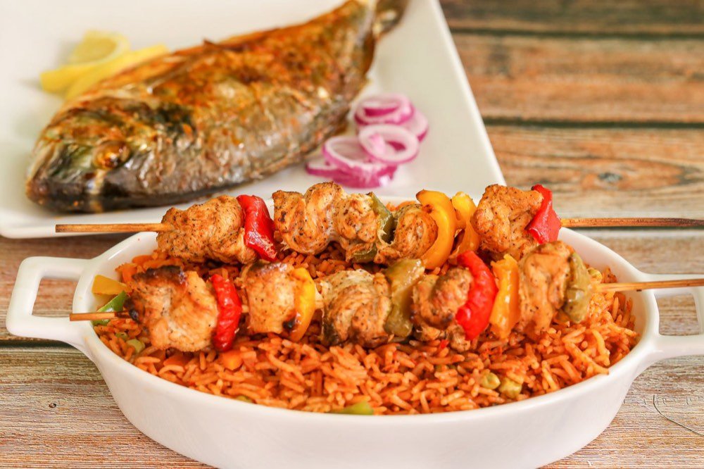 A West African plate of jollof rice with grilled chicken skewers and fish